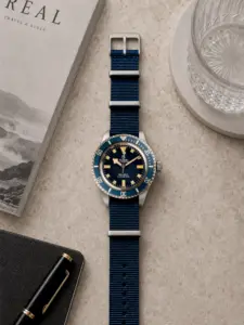 Dunkelblaues Nylon NATO Strap von vild Hamburg an einer Tudor Submariner Snowflake Taucheruhr, von oben mit stilvoller Tischdekoration fotografiert