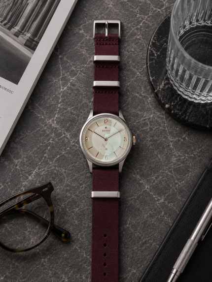 Dunkelrotes Stoff NATO Strap von vild Hamburg an einer Zenith Stellina Vintage, stilvoll von oben mit dekorativen Accessoires fotografiert
