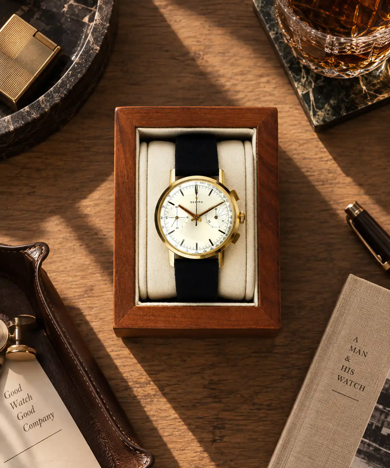 watch holder-wood-beige-motif-zenith-chrono-gold Wooden watch holder in walnut brown with beige cushion and Zenith gold chronograph placed on a wooden table with decoration.