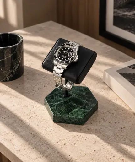 Watch stand with green marble and black leather cushion, and Rolex Submariner resting on a stone table with decorations