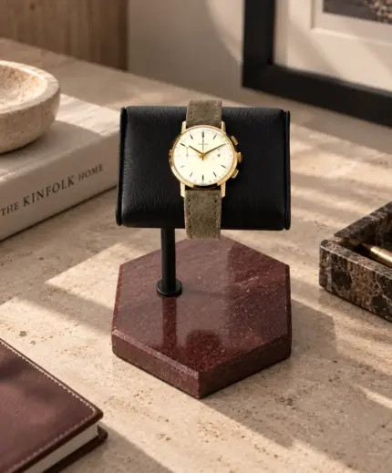 Watch stand with red marble and black leather cushion, and Zenith chronograph resting on a stone table with decorations