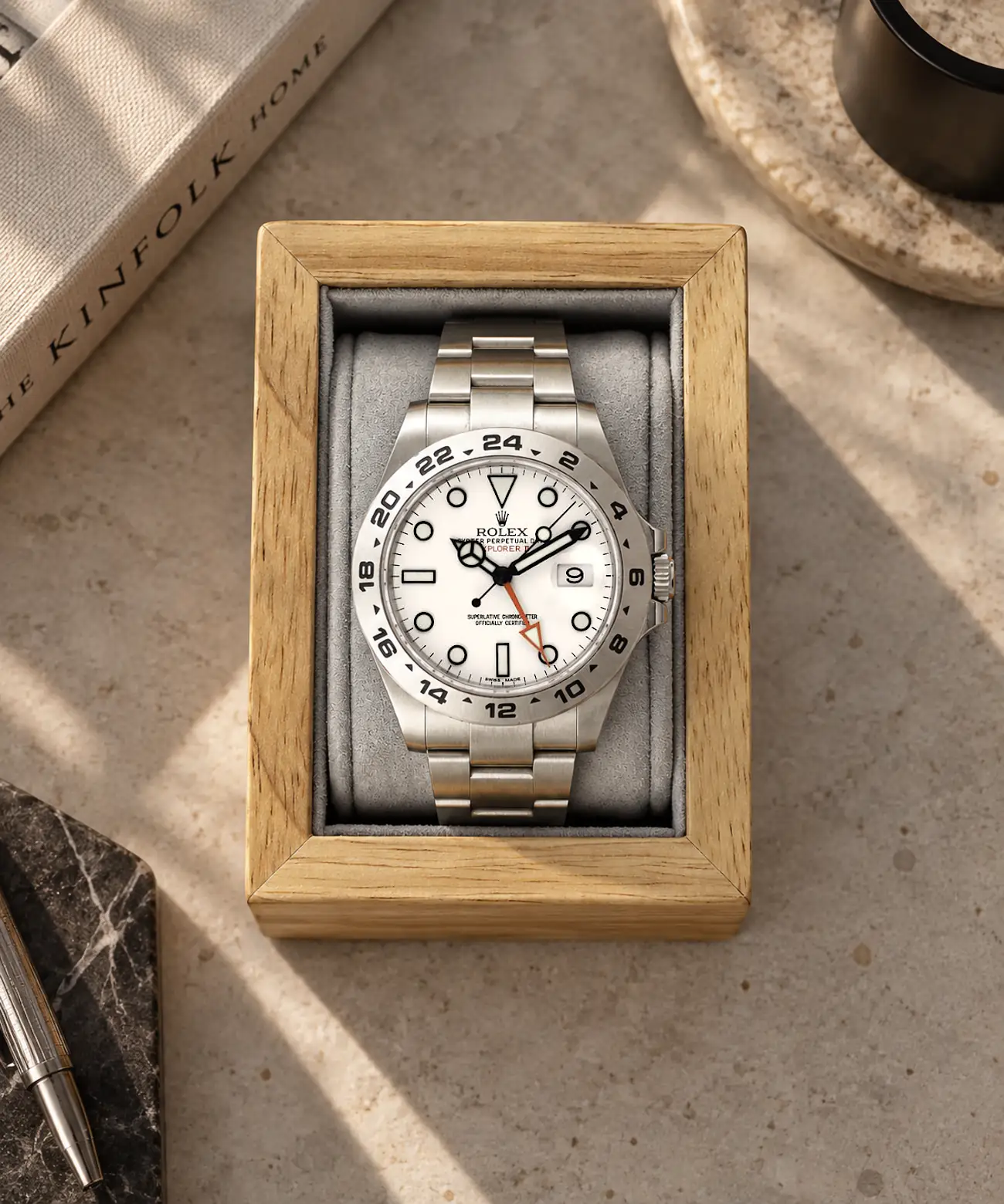 uhrenhalter-holz-hellgrau-motiv-rolex-explorer-ii Holz Uhrenhalter in Eiche Braun und hellgrauem Kissen mit Rolex Explorer II aufgelegt auf Steintisch mit Deko.