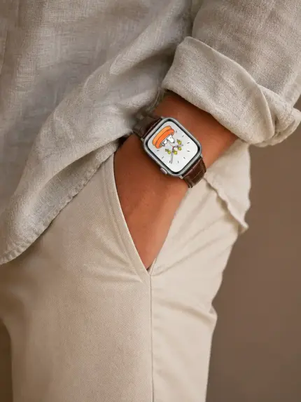 Mann in hellem Leinen Hemd und heller Chino steht vor Wand und hat die Hand in der Hosentasche. Er trägt eine silberne Apple Watch mit braunem Kroko Lederarmband von vild.