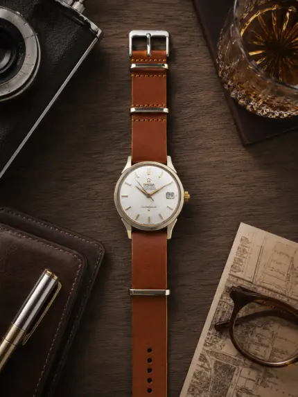 Hellbraunes Leder NATO Strap von vild Hamburg an einer Omega Constellation Vintage Ref. 168.004, fotografiert von oben auf einem dekorierten Tisch