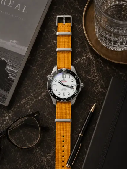Senffarbenes Premium NATO Strap von vild Hamburg an einer Omega Seamaster Diver 300M, stilvoll von oben mit Tischdekoration fotografiert
