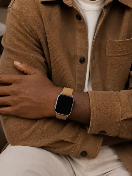 Mann in hellbrauner Stoff Jacke und weißem T-Shirt sitzt und trägt eine silberne Apple Watch mit hellbraunem Wildlederarmband von vild.