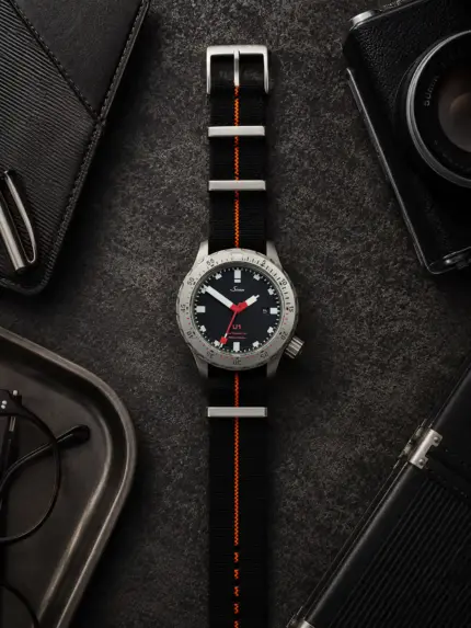 Scuba NATO Strap schwarz orange von vild Hamburg, an einer Sinn U1 montiert und von oben auf dekoriertem Tisch fotografiert