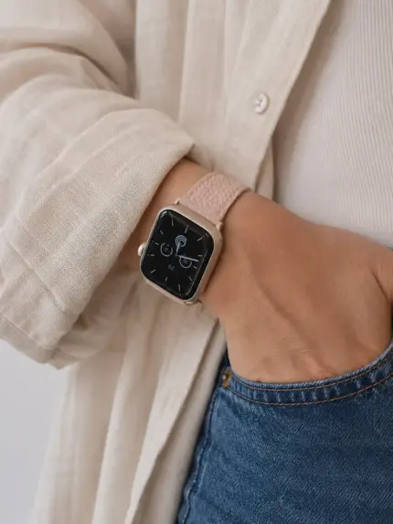 Frau in Leinen Hemd und blauer Jeans steht vor Wand mit Hand in der Hosentasche und trägt eine silber matte Apple Watch mit rosa Lederarmband von vild.