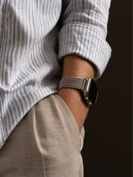Ausschnitt vom Handgelenk eines Mannes mit blauem Hemd und heller Stoffhose. Silberne Apple Watch mit grau-braunem Canvas Armband von vild an seinem Handgelenk.