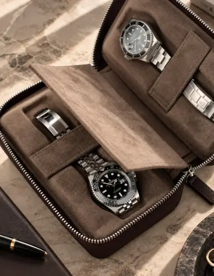 offenes Uhrenetui mit weichem grau-braunem Wildleder Inlet liegt auf Steintisch mit Kugelschreiber und Agenda. Rolex GMT Master II Bruce Wayne liegt festgeklippt in einem Slot. In dem zweiten Slot liegt eine Rolex Submariner Date festgeklippt.