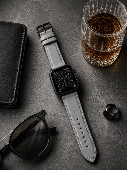Apple Watch leather strap in grey from vild Hamburg, mounted on the watch with sunglasses and decoration from above.