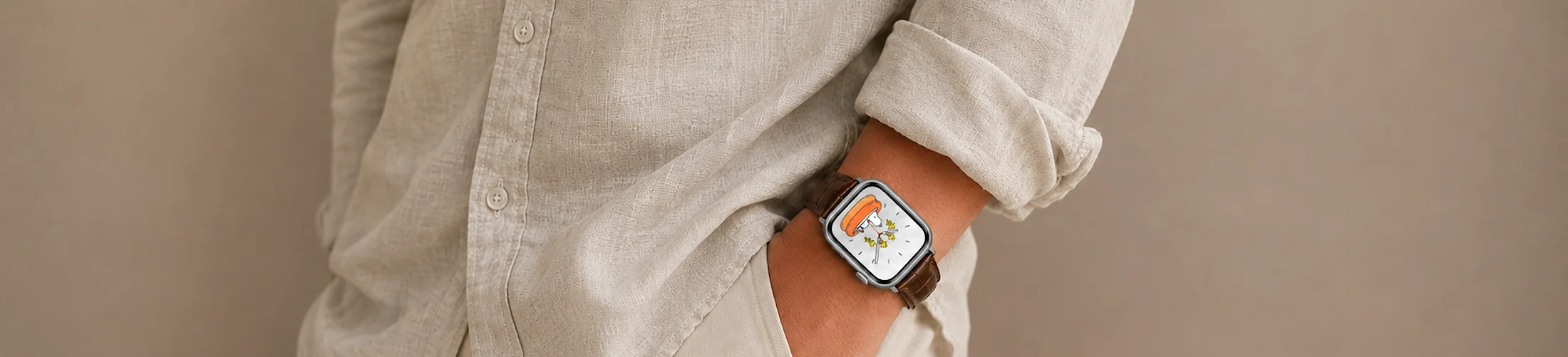 A man in a linen shirt and light chinos stands with his hands in his pockets in front of a wall, wearing a silver Apple Watch with a brown crocodile leather strap by vild