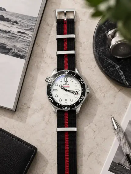 Premium NATO strap MISTRAL in black with red stripe by vild, mounted on an Omega Seamaster with a white dial and shown from above with matching table decoration