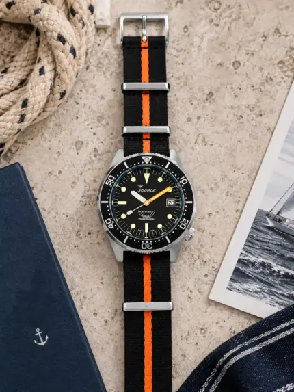 Premium fabric NATO strap SEAFARER in black with orange stripe by vild, mounted on a Squale with black dial and shown from above with matching table decoration