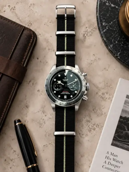 Nylon NATO strap SILVERSTONE in black with grey stripe by vild, mounted on a Tudor chronograph with black dial and shown from above with matching table decoration