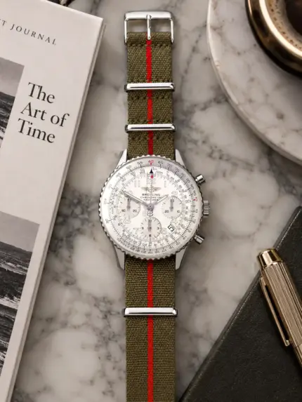 Premium NATO strap MONZA in olive with red stripe by vild, mounted on a Breitling Navitimer with white dial and shown from above with matching table decoration