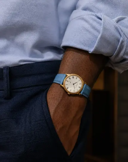 Leather watch strap in blue by vild Hamburg on a Patek Philippe Calatrava rose gold ref 5119R-001 worn on the wrist of a man with a light blue shirt and dark blue suit trousers.