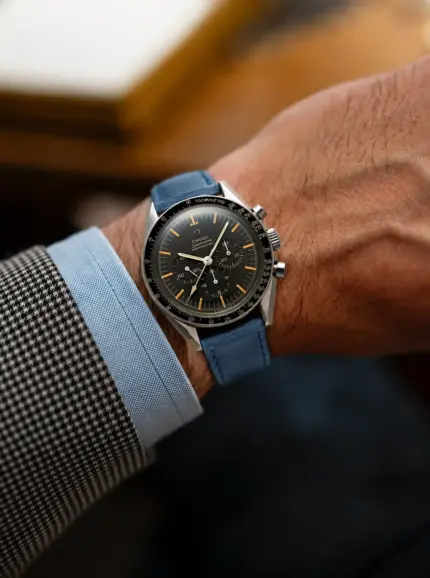 Blue leather watch strap from vild Hamburg on an Omega speedmaster professional moonwatch vintage on the wrist of a man wearing a light blue jacket and shirt.