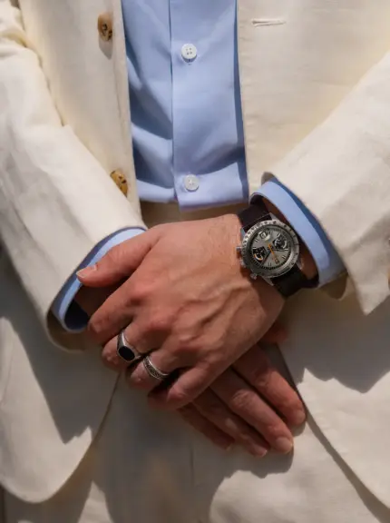 Dark brown leather watch strap by vild Hamburg on a Tudor Oysterdate Chronograph Monte Carlo, worn on the wrist of a man wearing a light jacket, light blue shirt and light suit trousers.