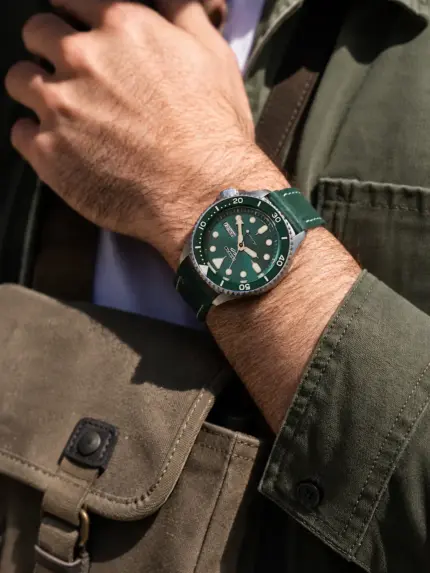 Green leather watch strap by vild Hamburg on a green Seiko Sports watch on the wrist of a man wearing a dark green denim jacket and carrying a shoulder bag.