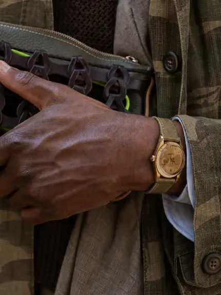 Green-brown leather watch strap from vild Hamburg on a vintage gold Rolex Datejust on the wrist of a man wearing a camouflage jacket and carrying a dark green bag