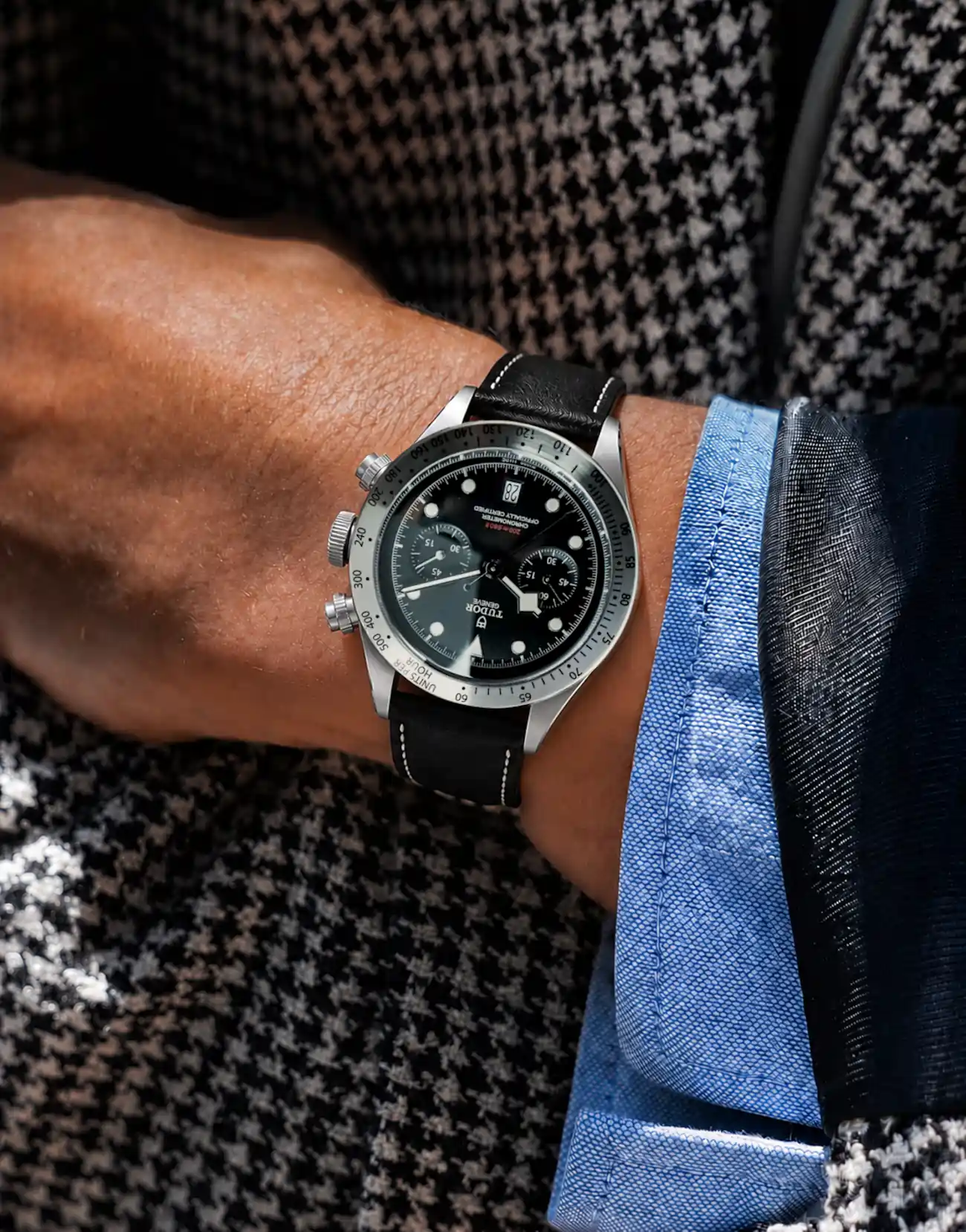Leather watch strap in black by vild Hamburg, worn on a Tudor Black Bay Chrono ref 79350-0002 on the wrist of a man wearing a black and white jacket.