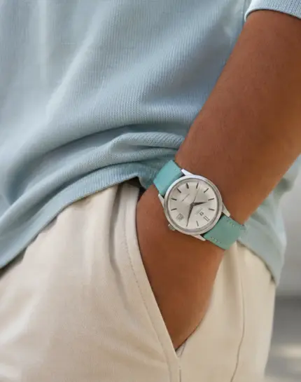 Leather watch strap in Tiffany turquoise by vild Hamburg worn on the wrist of a man wearing a blue knit shirt and light-colored trousers on an Omega Seamaster Quartz Vintage watch.
