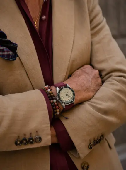 Dark red suede watch strap by vild Hamburg worn on the wrist of an Oris Divers Sixty-Five man wearing a brown blazer and a burgundy linen shirt.