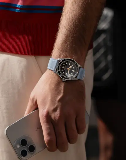 Light blue suede watch strap by vild Hamburg on a Tudor Black Bay Fifty-Eight ref 79030N, worn on the wrist of a man wearing light chinos and a red knit shirt.