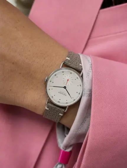 Vintage grey-brown leather watch strap by vild Hamburg, worn on a NOMOS Glashütte Metro neomatik watch on the wrist of a woman wearing a pink blazer